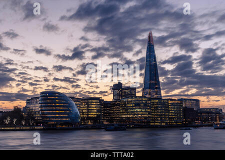 Low angle view of Shard London Bridge au milieu ville illuminée contre ciel nuageux pendant le coucher du soleil Banque D'Images