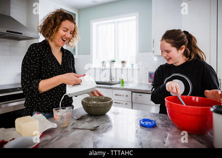 Mère fille avec mixer dans des bols sur l'île de cuisine à la maison Banque D'Images