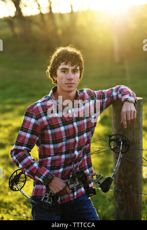 Portrait of teenage boy holding bow en se tenant sur le terrain au cours de journée ensoleillée Banque D'Images