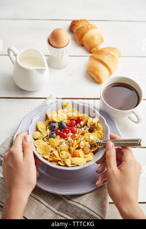 Les mains coupées de woman holding bowl avec des céréales de petit-déjeuner sur la table à la maison Banque D'Images