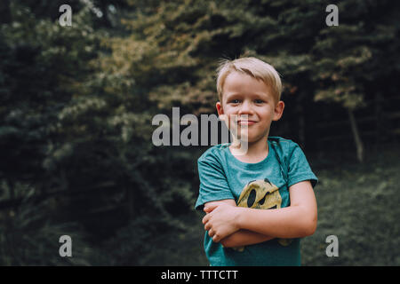 Portrait of boy with arms crossed standing at park Banque D'Images