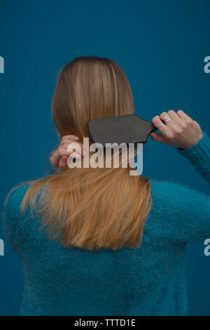 Vue arrière du woman brushing cheveux contre fond bleu Banque D'Images