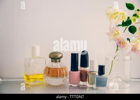 Produits de beauté organisé par vase à fleurs sur table contre mur blanc Banque D'Images