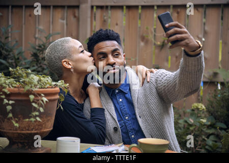 Woman kissing boyfriend tout en tenant en arrière-cour selfies Banque D'Images