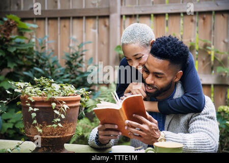 Happy woman embracing boyfriend reading book in backyard Banque D'Images