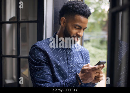 L'homme à l'aide de téléphone mobile tout en se tenant à l'entrée Banque D'Images