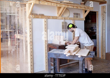 Vue latérale du carpenter wearing protection auditive tout en travaillant en atelier contre mur Banque D'Images