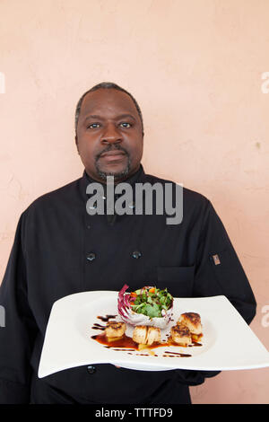 EXUMA, Bahamas. Le chef de l'Oiseau Cay Resort tenant un plat de pétoncles. Banque D'Images