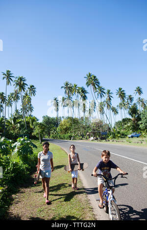 Moorea, Polynésie française. Les enfants de la planche à roulettes et le vélo. Banque D'Images