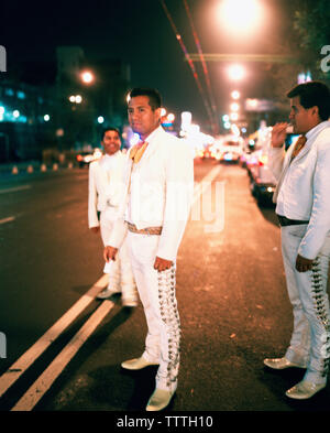 Mexique, Mexico, Mariachis debout sur la rue illuminée la nuit en attente pour les clients de l'embaucher pour jouer de la musique. Banque D'Images