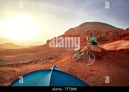 Randonneur le café tout en étant assis en VTT sur des roches dans le desert Banque D'Images