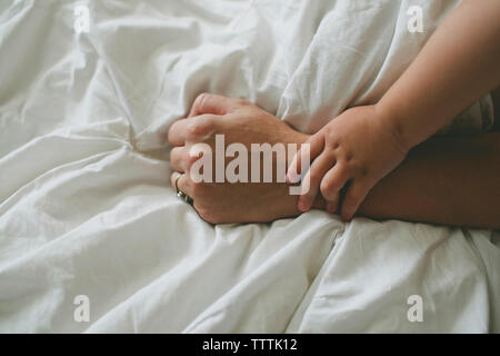 Portrait of boy holding mother's hand on bed Banque D'Images