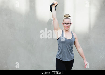 Portrait of woman lifting kettlebell contre le mur tout en exerçant Banque D'Images