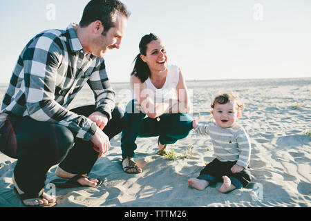 Portrait of cheerful fils avec les parents assis sur le sable à la plage Banque D'Images