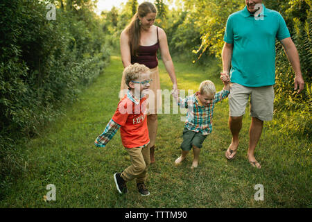 Heureux parents avec fils marche sur terrain herbeux en forêt Banque D'Images