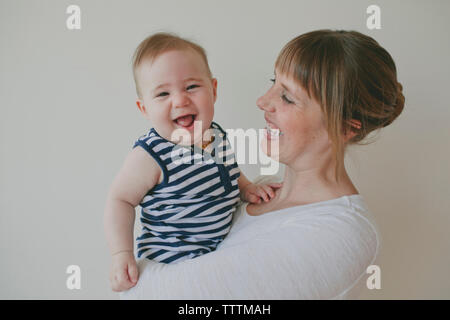 Portrait of cheerful fils porté par la mère contre fond blanc Banque D'Images