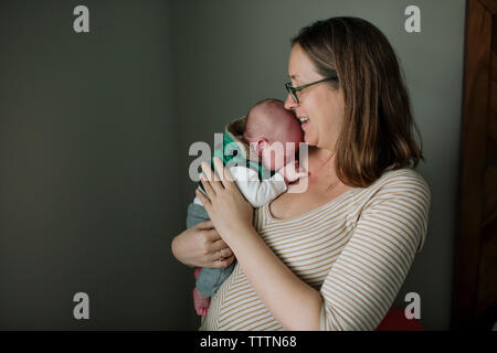 Smiling mother exerçant son fils nouveau-né en position debout contre le mur à la maison Banque D'Images