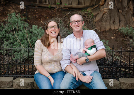 Portrait of happy parents avec newborn sleeping son sitting in park Banque D'Images