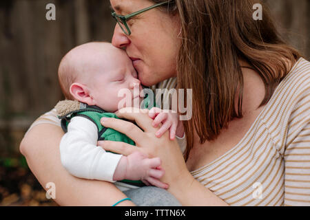 Close-up of loving mother kissing sleeping newborn son in park Banque D'Images