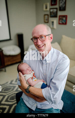 Portrait of smiling father carrying newborn sleeping cute son at home Banque D'Images