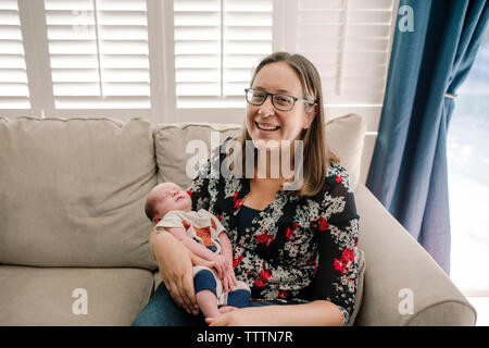 Portrait of smiling mother carrying newborn sleeping mignon fils alors qu'il était assis sur la table à la maison Banque D'Images