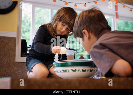 Sœur breaking egg dans le bol dans la cuisine Banque D'Images