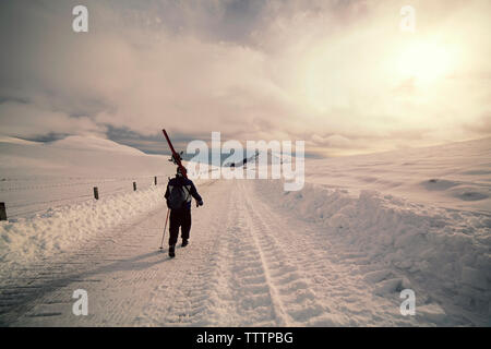 Vue arrière de l'homme marche sur Paysage de neige contre ciel nuageux Banque D'Images