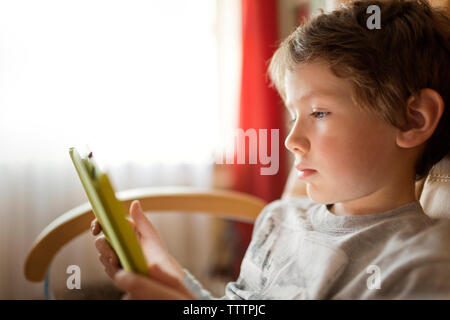 Boy using tablet computer tout en restant assis à la maison Banque D'Images