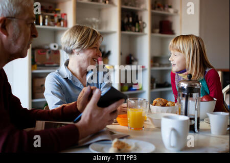 Grand-père à la petite-fille à parler à grand-mère tout en étant assis à table Banque D'Images