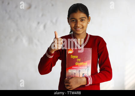 Schoolgirl holding a book and showing thumbs up sign Stock Photo