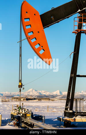 Close-up de pumpjack avec ses montagnes couvertes de neige et ciel bleu en arrière-plan, à l'ouest d'Airdrie, Alberta, Canada Banque D'Images