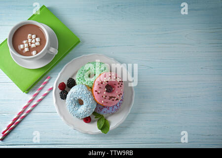 Plaque avec de délicieux donuts, baies et tasse de café sur la table en bois blanc Banque D'Images