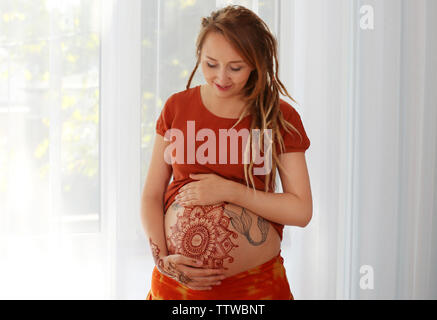 Jeune femme enceinte avec tatouage au henné sur le ventre sur un fond clair Banque D'Images