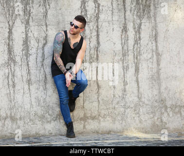 Jeune homme posant tatoué sur fond de mur de béton sale Banque D'Images