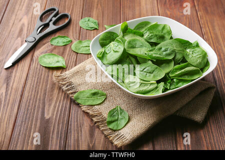 Bol en céramique pleine d'épinards frais, des ciseaux et de l'ensachage sur table en bois Banque D'Images