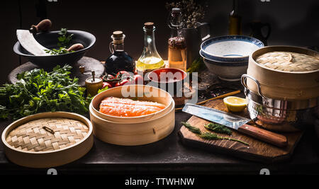 La cuisine asiatique . Bateau à vapeur de bambou avec filet de saumon sur sombre cuisine rustique avec divers outils, assaisonnement, et d'ingrédients . La cuisson de la préparation. Cui asiatique Banque D'Images