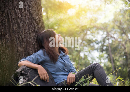 Happy woman profiter et se détendre avec la nature. Belle Jeune femme assise sous le grand arbre en vert forêt. Banque D'Images