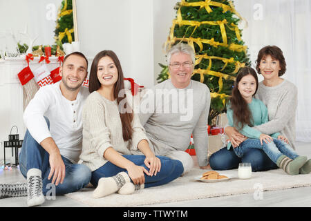 Une famille heureuse avec des biscuits et du lait dans la salle de séjour décorée pour Noël Banque D'Images