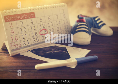 Calendrier avec mark, échographie photo de bébé et chaussures enfants sur la table Banque D'Images