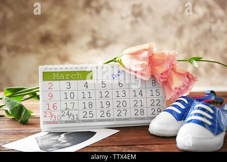 Calendrier avec mark, échographie photo de bébé et chaussures enfants sur la table Banque D'Images