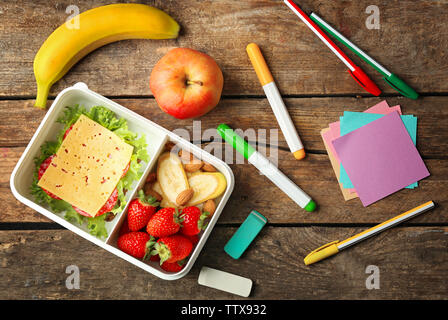 Boîte à lunch avec des aliments et de papeterie sur fond de bois, vue du dessus Banque D'Images