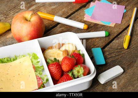 Boîte à lunch avec des aliments et de papeterie sur fond de bois Banque D'Images