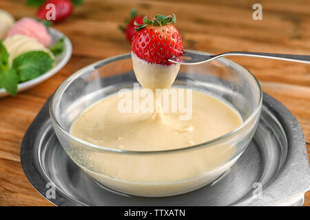 Fourche avec des fraises fraîches trempées dans la fondue au chocolat blanc, gros plan Banque D'Images