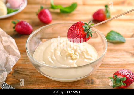 Des fraises fraîches trempant dans la fondue au chocolat blanc sur la table Banque D'Images