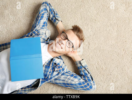 Beau jeune homme avec book lying on carpet Banque D'Images