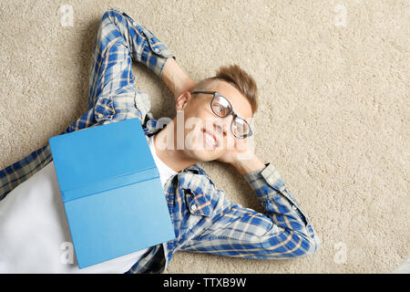 Beau jeune homme avec book lying on carpet Banque D'Images