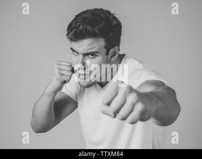 Jeune homme séduisant en rage à la position de défense en furieux et menacer avec perforation en poing en colère et bouleversé l'expression visage fou ba gris isolé Banque D'Images