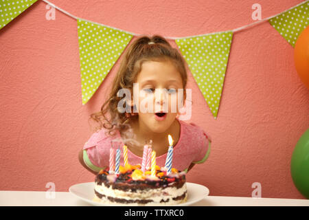 Funny little girl blowing out candles on cake at home Banque D'Images