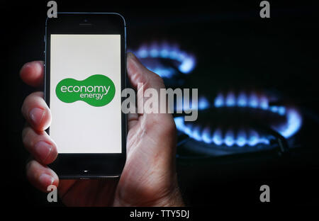 Un homme à la recherche sur le site web logo pour entreprise de l'énergie Énergie Économie sur son téléphone devant sa cuisinière à gaz (usage éditorial uniquement) Banque D'Images