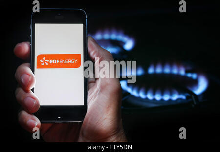 Un homme à la recherche sur le site web logo pour société d'énergie de l'énergie EDF sur son téléphone devant sa cuisinière à gaz (usage éditorial uniquement) Banque D'Images